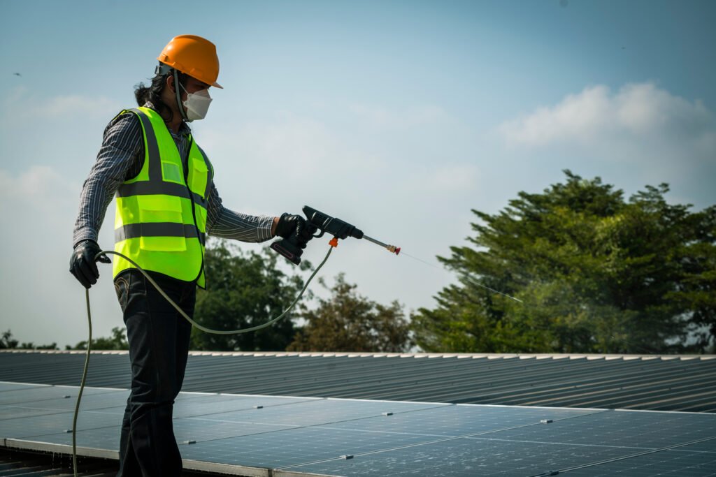 Maintenance technician using high pressure water to clean the solar panels that are dirty with dust to improve the efficiency of solar energy storage.